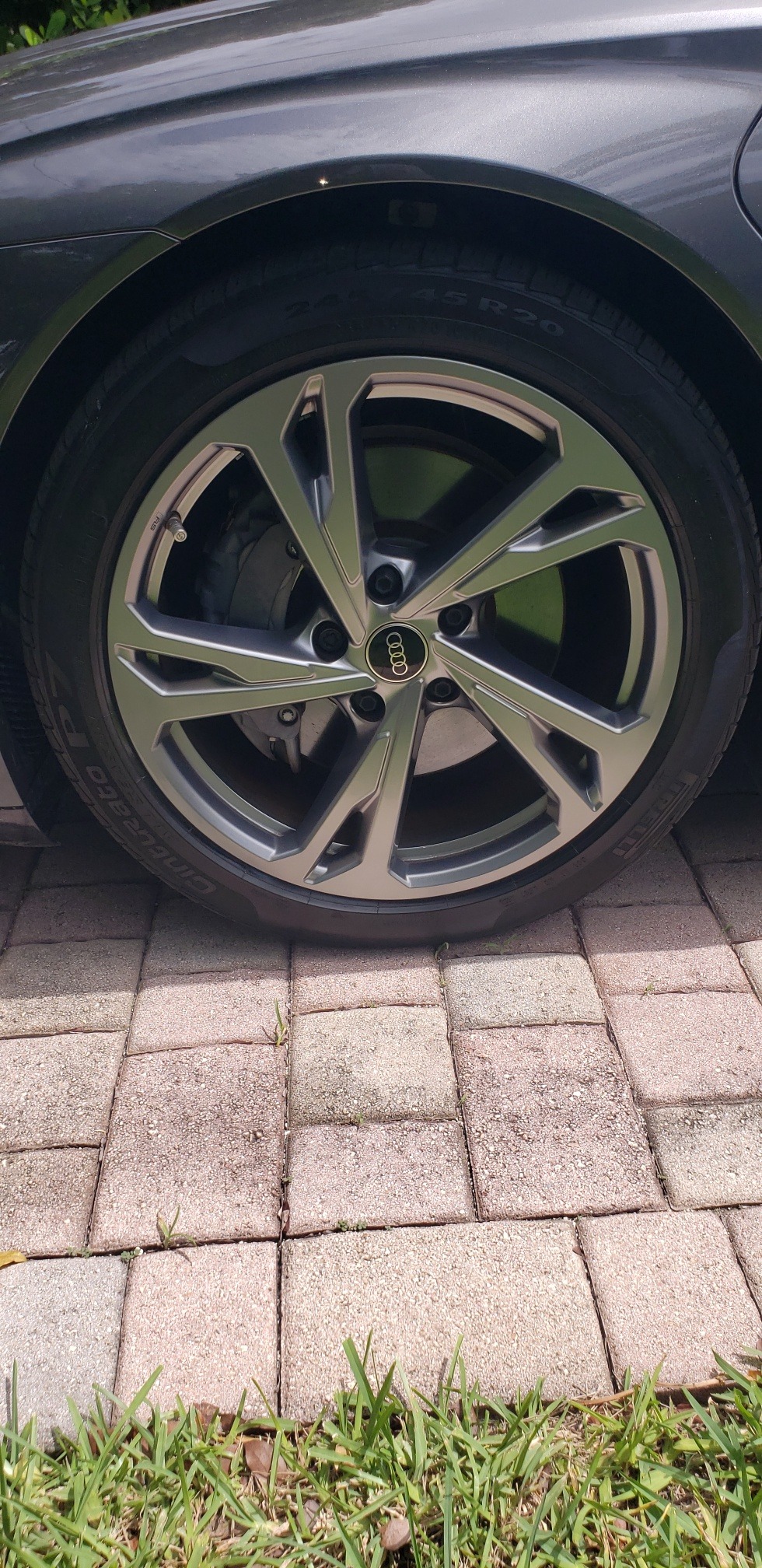 Flat tire on a sleek black Audi, showcasing a detailed wheel with modern design, parked on a patterned brick surface with grass.