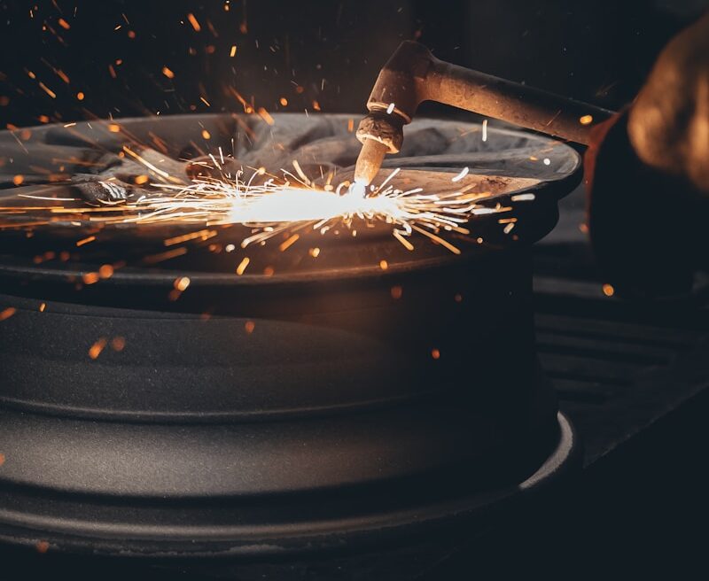 A welding torch emits bright sparks while fusing metal components on a black wheel rim, illustrating the process of metal fabrication.
