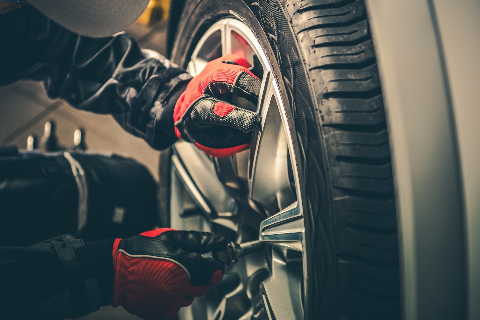 A mechanic in red gloves is tightening a wheel nut on a silver car, emphasizing the importance of proper tire maintenance.